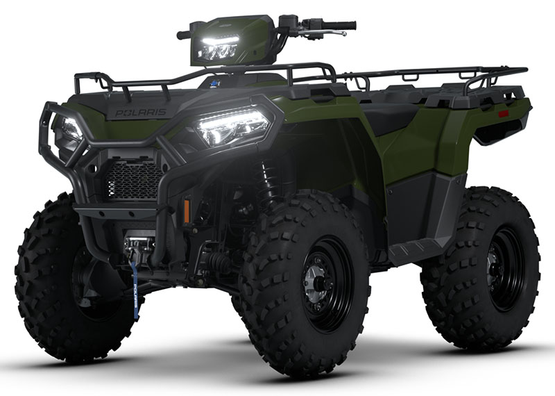 A green Polaris all-terrain vehicle (ATV) with large rugged tires, front and rear cargo racks, headlights on, and a sturdy build, designed for off-road use.