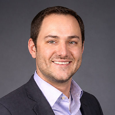 Headshot of a smiling man in a dark suit jacket and light-colored button-down shirt.